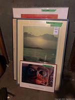 Photo of four framed artworks stacked against a wall, showing sizes and labels on frames.