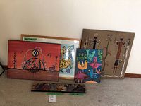 Five grouped artworks including Richard Packo painting and various Indigenous style painted panels and framed art against a wall.