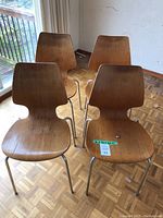 Four wooden chairs with tubular metal legs arranged on parquet floor near sliding door