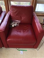 Front view of the red leather armchair with visible seat cushion and bag of felt pads on the seat.