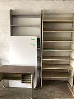 View of wooden shelving unit, metal shelving unit, white table top, and metal desk with wood finish in garage setting