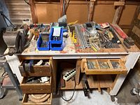 Wide shot of workbench with various hand tools and large clamp placed on top, drawers and tool tray visible.