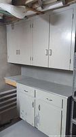Left side view of two white wall cabinets stacked vertically showing handles and wear on surfaces