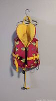 Red and yellow kids flotation vest with fish print, adjustable straps and buckles hung on a hanger