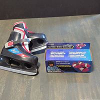 Photo of one pair of black and red youth ice skates with adjustable size 8-9 showing buckles and velcro straps, and a blue boxed set of Patins-Bob skate lace ties.