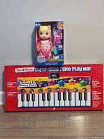 Photo shows the 6-foot long Super-Sized Piano Play Mat in original packaging and a boxed Baby Alive doll with accessories.