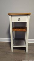 Front view of kitchen side table showing wooden top, drawer with metal knob, adjustable wooden shelf in the middle, and metal wine rack shelf at the bottom.