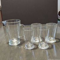 Photo showing one glass pitcher and four long drink glasses with embossed bumblebee motif, all with solid bases for stability, placed on a reflective surface.