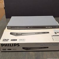 Silver Philips DVD player unit displayed on top of its original retail box showing front panel and buttons clearly.