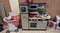 Full view of wooden play kitchen and plastic shopping cart loaded with accessories