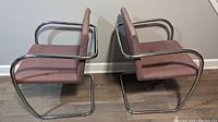 Side profile view of two retro chairs showing chrome tubular frame and dusty rose upholstery on seat and back.