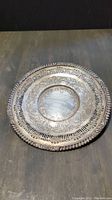 Decorative round silver plate showing ornate floral embossing and pierced border.