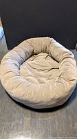 Beige circular dog bed, plush fabric surface, lightly used.