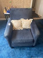 Front view of blue upholstered armchair with two decorative cream pillows on seat, showing condition and style