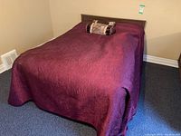 Bed fully made up with burgundy bedspread and decorative pillows showing the headboard and footboard in place.
