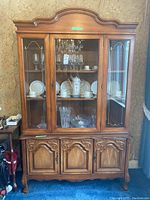 Front view of the wood buffet hutch's upper glass cabinet with dishware inside and the lower cabinet with carved wooden doors.