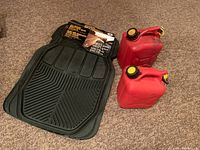 Four Tune It brand all season heavy duty rubber car mats and two small red plastic jerry cans placed on carpeted floor.