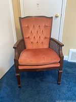 Front view of wooden armchair with orange tufted upholstery and cane sides, showing button tufting detail and cushioned seat.