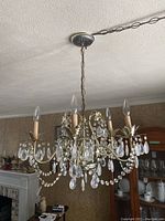 Chandelier hanging from ceiling showing all five candle-style bulb holders with attached crystal decorations and brass arms.