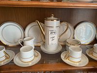 Wide view of porcelain coffee set with gold trim including coffee pot, cups, saucers, plates, creamer, and sugar bowl.