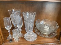 Full view of all glass and crystal pieces displayed on shelf, showing varying sizes and shapes including vases, bowls, plates, and glasses.