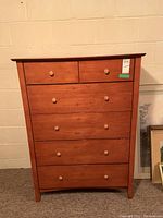 Front view of medium brown wooden dresser with six drawers and round wooden knobs, showing slight scratches.