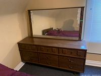 Front view of wooden dresser with nine drawers and attached large mirror in a bedroom corner.