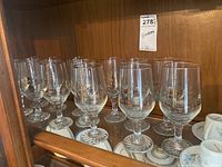 Shelf of 13 clear beer glasses featuring Olympic rings design on the bowl, stemmed base visible