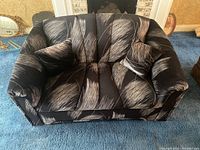 Front view of the retro patterned love seat with two matching throw pillows on a blue carpet.