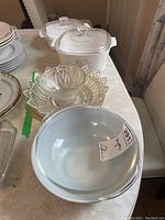 Photo showing 9-inch Pyrex bowl, two white casserole dishes with lids, assorted clear glass pie plates and bowls, stacked plates in background