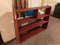 Front angled view of the painted wood shelving unit showing shelves, surface wear, and reddish paint finish.