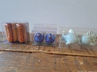 Three boxed sets of salt and pepper shakers on wooden surface: hot dog design, blue bird design, fish design
