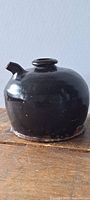 Front view photo showing black glazed ceramic soy jug on wooden surface.
