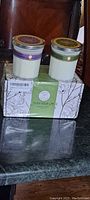 Two aromatherapy scented candles on top of the packaging box showing Twilight Lavender and Fig & Fir labels with decorative lids and design on the box.
