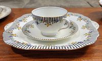 Top side view of cake plate with teacup and saucer stacked showing detailed floral and black striped pattern on white bone china