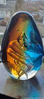 Front view of egg-shaped blue and gold glass paperweight showcasing internal swirl design and bubbles.
