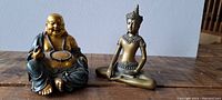 Front view of two Buddha figurines, a Laughing Buddha and a meditative Buddha, on a wooden surface.