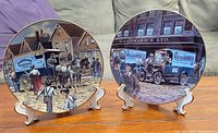 Two Woodward's collectible plates shown on white display stands, featuring horse-drawn carriage and vintage truck artwork.