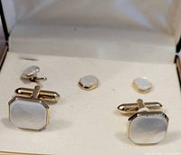 Set of gold toned cufflinks and tie pins with faux mother of pearl insets displayed in a fabric lined case.