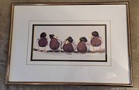 Photo of the framed print showing six ducks standing in a row facing backward, the print is matted and framed with a light metallic frame.