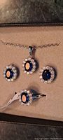 Close up photo of costume jewelry set with earrings, ring, and necklace all featuring blue oval stones surrounded by white rhinestones on silver tone metal.