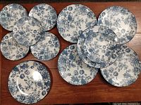 Top view of 12 plates arranged on wood surface, showing blue floral pattern on white ceramic.