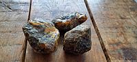 Three pieces of raw amber on wooden surface showing natural rough texture and colors