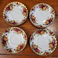 Four Royal Albert Old Country Roses bone china saucers laid out on a wooden surface, showing floral pattern and gold trim detail