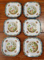 Top view of all six square side plates displaying the colorful bird and floral pattern with ornate blue and gold rim.