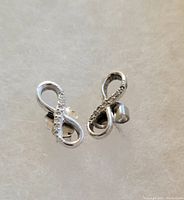 Photo showing pair of infinity-shaped sterling silver earrings with clear stones and butterfly clasps