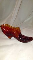 Amberina glass shoe figurine shown from front-side angle, highlighting red and yellow gradient and textured design.