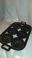 Front angled view of antique cast iron muffin baking tray showing six scalloped molds and handles.