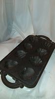 Side angled view of cast iron baking tray showing fruit and vegetable mold shapes and one handle