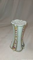 Porcelain hat pin holder, white base with hand-painted small flowers on vertical panels, gold accents, and top holes for pins.